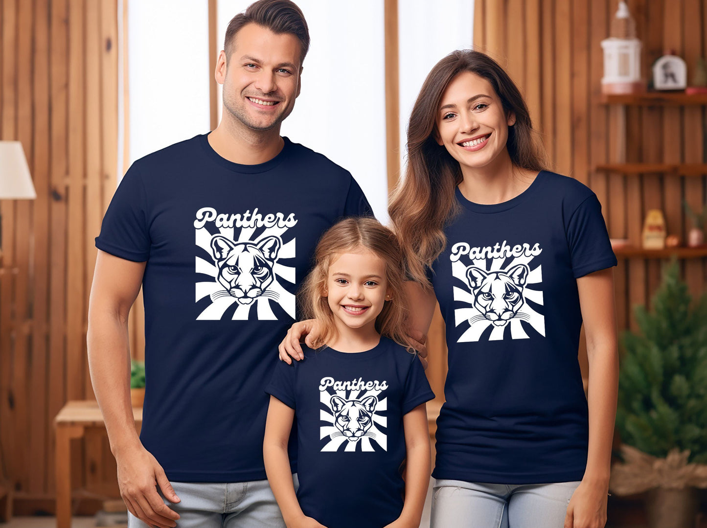 A family of three wearing matching navy blue t-shirts with a white panther graphic and the word 'Panthers' on the front, standing together in a cozy, wood-paneled room.
